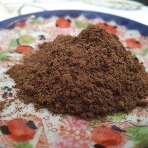 May include: A close-up of a pile of dark brown cocoa powder on a decorative plate with red and white floral designs.