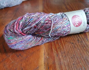 May include: A skein of multi-colored yarn with a brown label that says "Woonky's Yarn". The yarn is a mix of red, pink, purple, blue, green, and white.