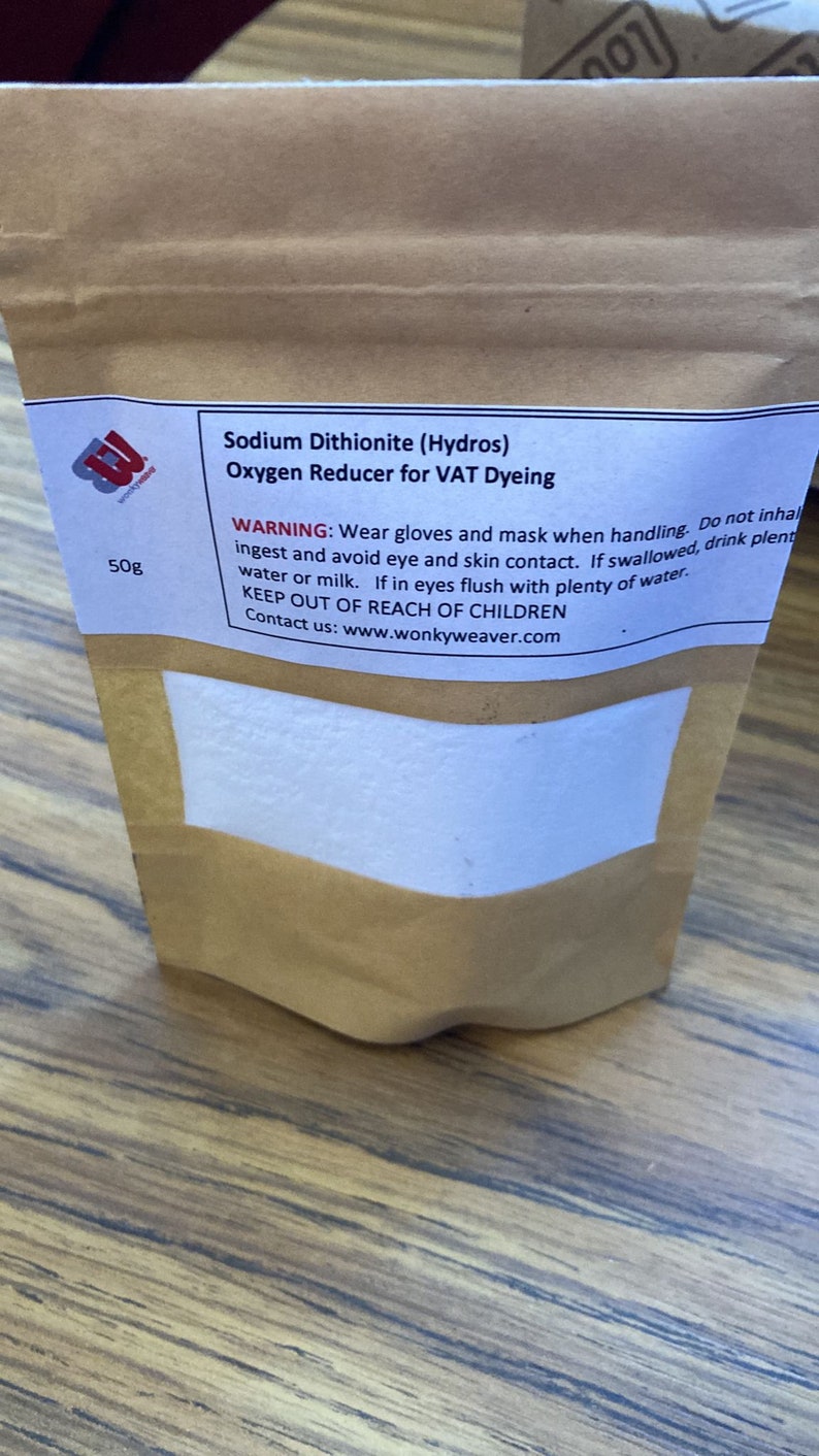 May include: A brown paper bag with a white label that reads "Sodium Dithionite (Hydros) Oxygen Reducer for VAT Dyeing". The label also includes a warning to wear gloves and a mask when handling the product, and to keep it out of reach of children. The bag contains a white powder and is labeled with a weight of 50g.