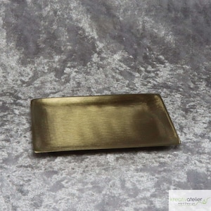 Könnte beinhalten: Ein rechteckiges, goldfarbenes Tablett aus Metall mit gebürsteter Oberfläche. Das Tablett befindet sich auf einer grauen, strukturierten Oberfläche.