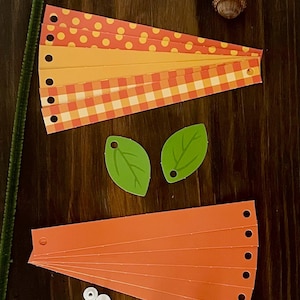 Pode incluir: Um kit de artesanato para fazer uma ab&oacute;bora. O kit inclui tiras de papel laranja, amarelo e vermelho com bolinhas e padr&otilde;es xadrez, folhas de papel verde, olhos saltitantes brancos e um limpador de cachimbo marrom.