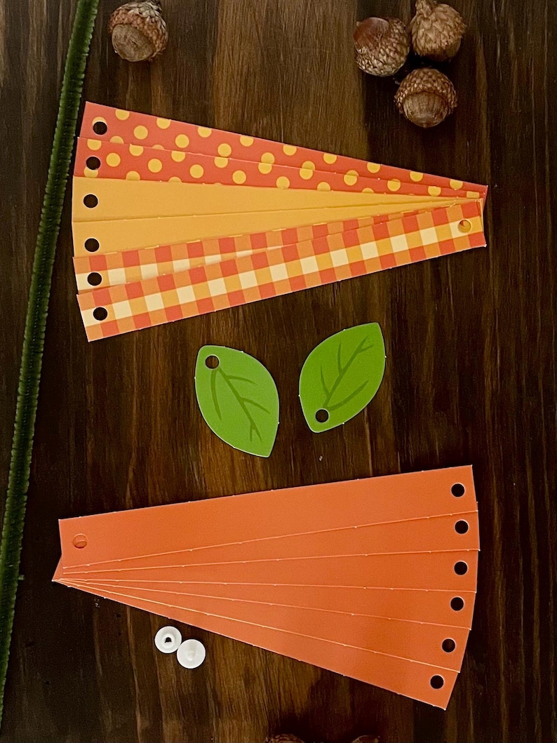 Pode incluir: Um kit de artesanato para fazer uma ab&oacute;bora. O kit inclui tiras de papel laranja, amarelo e vermelho com bolinhas e padr&otilde;es xadrez, folhas de papel verde, olhos saltitantes brancos e um limpador de cachimbo marrom.
