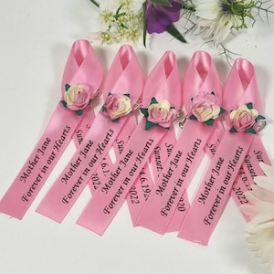 May include: Pink satin ribbon favours with a small flower embellishment and the text "Mother Jane Forever in our Hearts" printed on each ribbon.
