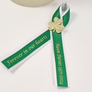 May include: Green and white ribbon with a gold shamrock. The ribbon has the text "Forever in our hearts" and "Jason Davies 1977-2024" printed on it.