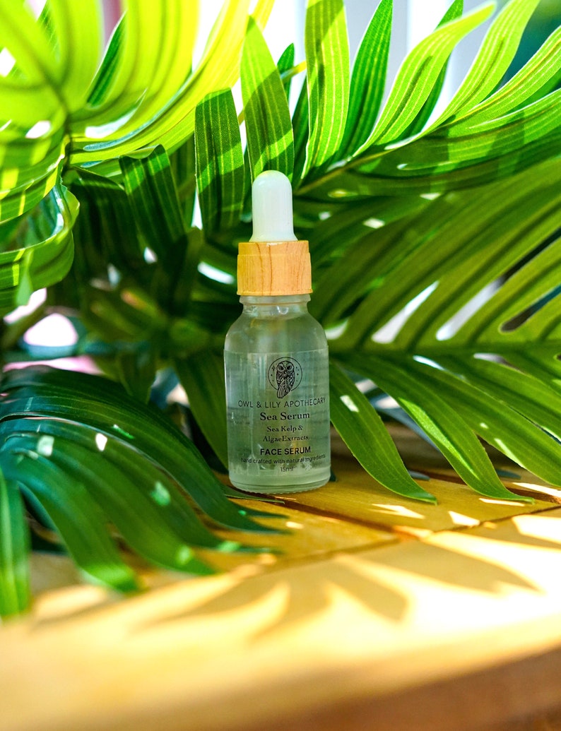 May include: A clear glass bottle with a wooden cap and dropper. The bottle contains a face serum with the text "Owl & Lily Apothecary Sea Serum Sea Kelp & Algae Extracts Face Serum" on the label.