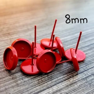 May include: A close-up of eight red 8mm earring settings with posts. The settings are scattered on a wooden surface.