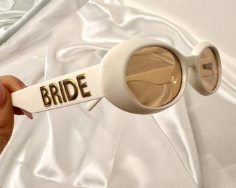 Gafas de novia, gafas de sol ovaladas color crema con detalle dorado de "Bride", accesorio para despedida de soltera.