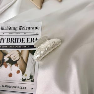 Add a touch of bridal sparkle to your special day with our pearlised diamanté “Bride” claw clip — the perfect accessory for any bride-to-be! Grab your girls and get hen party ready with our simply stunning, on trend, bride claw clip!