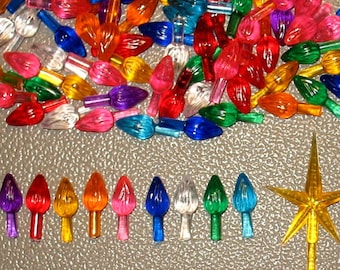 May include: A large assortment of colorful Christmas light bulbs in various shades of red, orange, yellow, green, blue, and purple. The bulbs are arranged in a pile, with a few individual bulbs displayed below. The bulbs are all in the shape of a teardrop, with a small metal tip at the bottom.
