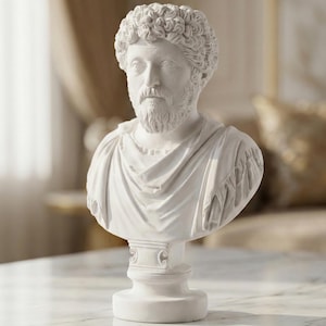 Könnte beinhalten: Eine weiße Büste eines Mannes mit lockigem Haar und Bart. Die Skulptur zeigt einen römischen Kaiser mit einem drapierten Gewand über den Schultern. Die Büste ist auf einem Sockel montiert und wahrscheinlich aus Gips oder einem ähnlichen Material gefertigt.