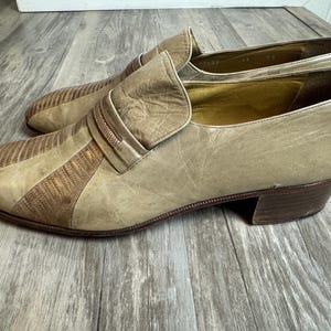 May include: A pair of vintage beige leather loafers with a textured, striped design on the toe and a small heel. The shoes have a slip-on style with a decorative strap across the top.