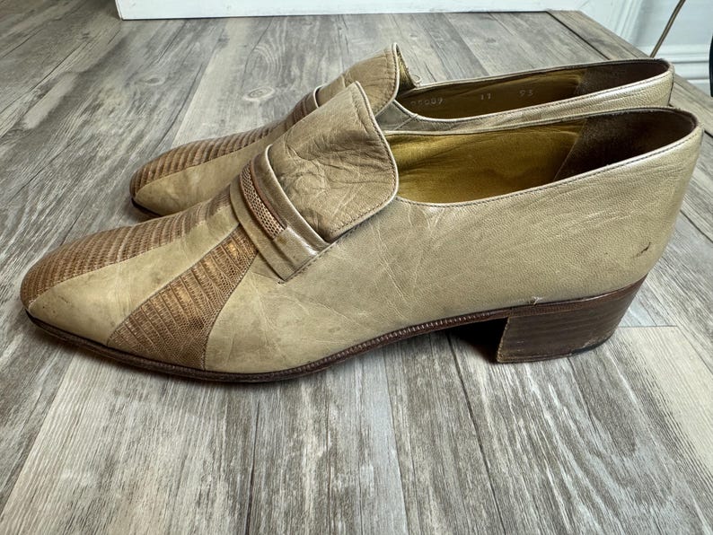 May include: A pair of vintage beige leather loafers with a textured, striped design on the toe and a small heel. The shoes have a slip-on style with a decorative strap across the top.
