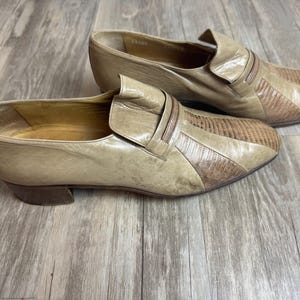 May include: A pair of vintage tan leather slip-on shoes. The shoes have a textured design on the toe and a small heel. The shoes are in a used condition.
