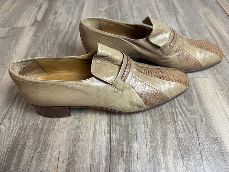 May include: A pair of vintage tan leather slip-on shoes. The shoes have a textured design on the toe and a small heel. The shoes are in a used condition.