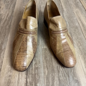 May include: A pair of vintage tan leather loafers. The shoes feature a textured, reptile-like pattern on the toe and a decorative strap across the top. The shoes are in good condition and appear to be unworn.