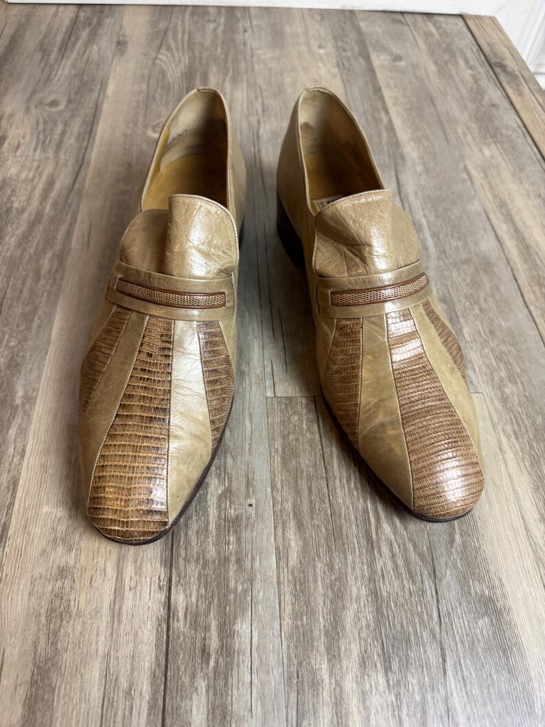 May include: A pair of vintage tan leather loafers. The shoes feature a textured, reptile-like pattern on the toe and a decorative strap across the top. The shoes are in good condition and appear to be unworn.