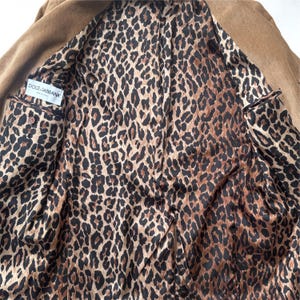 May include: A tan blazer with a leopard print lining. The interior features a brown and black animal print. The label "DOLCE&GABBANA MADE IN ITALY" is visible inside the jacket.