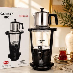 May include: A Golda Inc samovar featuring a clear glass water reservoir, a black base with a spigot, and a stainless steel teapot on top. The packaging box displays the brand name, the model number G183-074, and the text 4.5L Glass German Design.