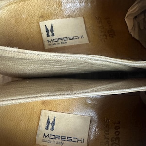 May include: Close-up of the inside of two beige leather shoes. The shoes have a textured surface and feature the brand name "MORESCHI" and "made in Italy" on a label. The text "Brass Boot" is also visible.