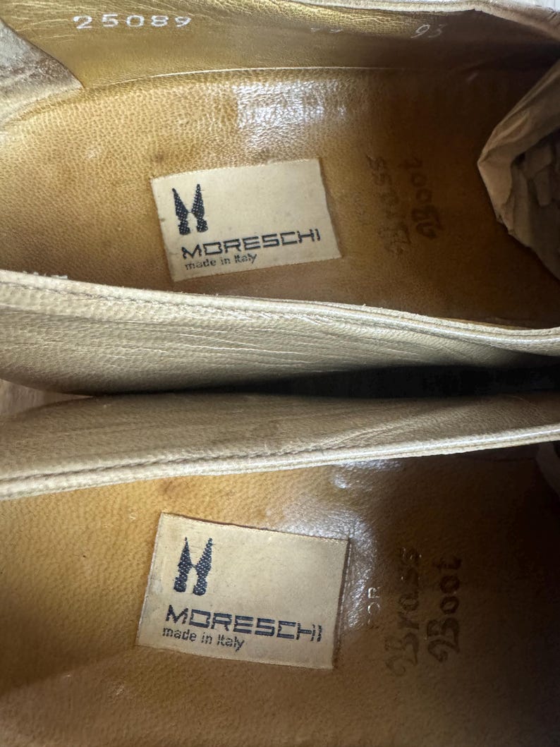 May include: Close-up of the inside of two beige leather shoes. The shoes have a textured surface and feature the brand name "MORESCHI" and "made in Italy" on a label. The text "Brass Boot" is also visible.
