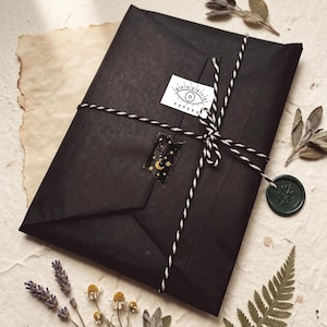 May include: A rectangular package wrapped in black paper, tied with black and white baker's twine. A white sticker with an eye illustration and the text "PAPERS" is attached. A dark green wax seal with a leaf imprint hangs from the twine.