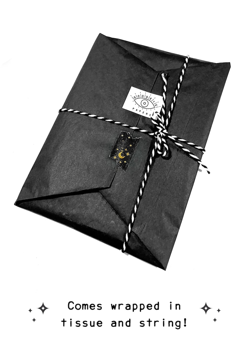 May include: A black parcel wrapped in tissue paper and tied with black and white twine. A sticker with an eye design and the word "PAPERS" is on the package. A gold and black sticker with a moon and stars is also on the package.