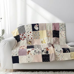 Peut inclure: Une courtepointe patchwork sur un canapé blanc. La courtepointe est composée de carrés de tissu aux couleurs pastel, avec des motifs floraux, rayés et de personnages. Le design comprend des carrés avec Minnie Mouse et d'autres personnages de dessins animés.