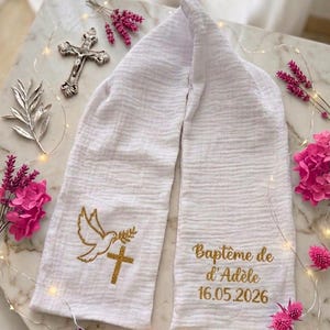 Peut inclure: Écharpe de baptême blanche avec broderie dorée d'une colombe, d'une croix et de texte. Le texte indique "Baptême de d'Adèle 16.05.2026". Entourée de fleurs roses et d'une croix argentée.