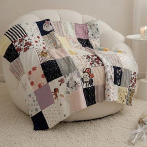 Peut inclure: Une couverture patchwork drapée sur une chaise blanche. La couverture présente une variété de carrés à motifs, notamment des motifs floraux et à rayures. La palette de couleurs comprend du rose, du jaune, du noir et du blanc.