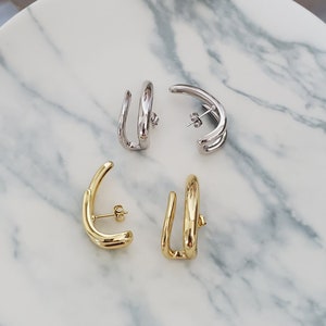 May include: Four gold and silver hoop earrings on a white marble surface. The earrings are all different shapes and sizes.