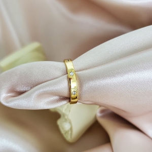 May include: A gold band ring with small clear stones set into the band.