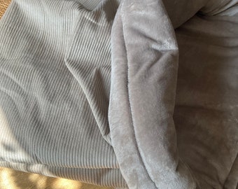 May include: A gray corduroy and plush pet bed with a soft, cozy interior. The bed is designed to provide comfort and warmth for pets.