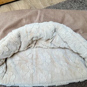 Può includere: Un letto per cani beige con uno strato esterno in velluto a coste marrone e uno strato interno morbido e soffice con un design a forma di zampa.