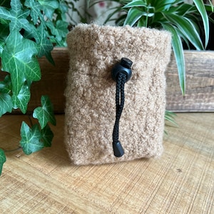 Könnte beinhalten: Eine kleine, braune, flauschige Kordeltasche mit einem schwarzen Band und einem Knopf.