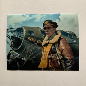 May include: A photograph of a man in a vintage aviator uniform, standing before a World War II-era bomber aircraft. The aircraft is olive green with the words "Wild Cat" painted on the side. The photo is signed.