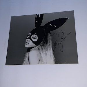 Puede incluir: Foto en blanco y negro de una mujer con una máscara de conejo negra y una firma debajo. La mujer tiene el pelo largo y rubio y mira hacia un lado.