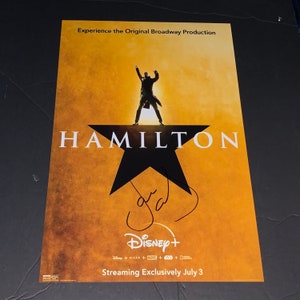 Puede incluir: Un póster amarillo con una estrella negra y el texto "HAMILTON" en letras blancas grandes. Una silueta de una persona de pie sobre la estrella con los brazos levantados. El texto "Experience the Original Broadway Production" está en la parte superior del póster. El texto "Disney+" está en la parte inferior del póster con el texto "Streaming Exclusively July 3".