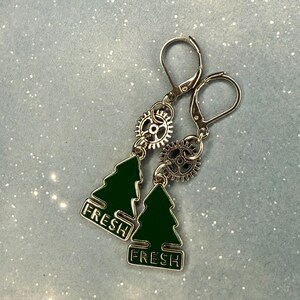 K&ouml;nnte beinhalten: Silberfarbene Ohrringe mit Steampunk-&Auml;sthetik. Jeder Ohrring hat einen kleinen, dunkelgr&uuml;nen Weihnachtsbaum-Anh&auml;nger mit dem Wort "FRESH" in wei&szlig;er Schrift. Der Baum-Anh&auml;nger h&auml;ngt unter einem silbernen Zahnrad.