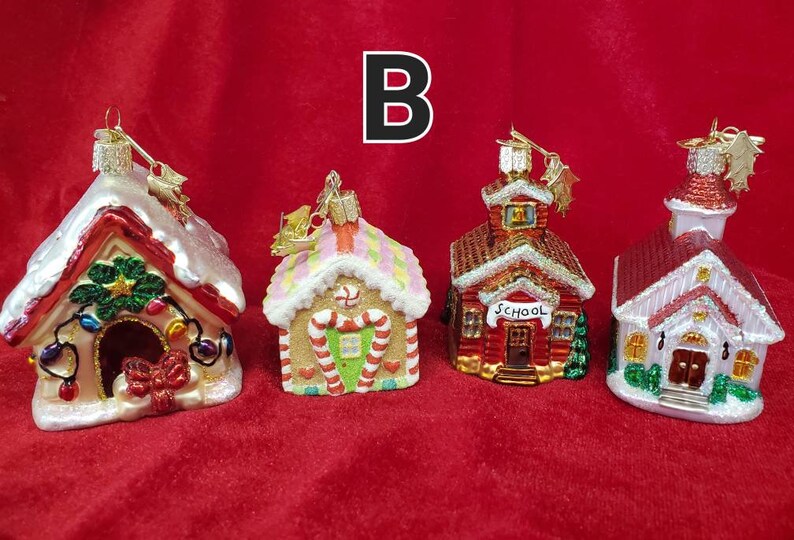 K&ouml;nnte beinhalten: Vier gl&auml;serne Weihnachtsbaumschmuckst&uuml;cke in Form von H&auml;usern. Die Schmuckst&uuml;cke sind mit Glitzer, Zuckerstangen und anderen festlichen Details verziert. Die H&auml;user umfassen ein Lebkuchenhaus, ein Schulhaus, eine Kirche und ein Hundehaus.