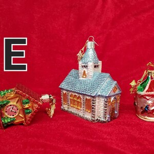 K&ouml;nnte beinhalten: Drei gl&auml;serne Weihnachtsbaumschmuckst&uuml;cke in Form von Geb&auml;uden. Das erste ist ein roter und gr&uuml;ner Glockenturm, das zweite ist eine blaue und wei&szlig;e Kirche und das dritte ist ein rotes, gr&uuml;nes und wei&szlig;es Karussell.
