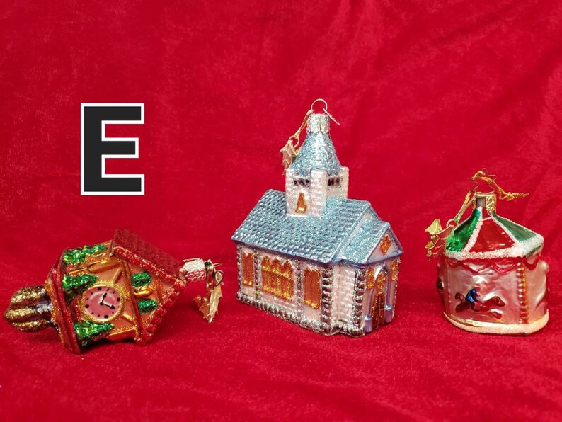 K&ouml;nnte beinhalten: Drei gl&auml;serne Weihnachtsbaumschmuckst&uuml;cke in Form von Geb&auml;uden. Das erste ist ein roter und gr&uuml;ner Glockenturm, das zweite ist eine blaue und wei&szlig;e Kirche und das dritte ist ein rotes, gr&uuml;nes und wei&szlig;es Karussell.