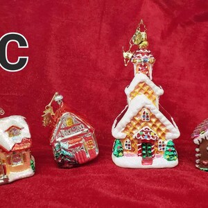 K&ouml;nnte beinhalten: Vier gl&auml;serne Weihnachtsbaumschmuckst&uuml;cke in Form von H&auml;usern. Die Schmuckst&uuml;cke sind mit Lebkuchendetails, Zuckerstangen und Schnee verziert. Die Schmuckst&uuml;cke befinden sich auf einem roten Hintergrund.