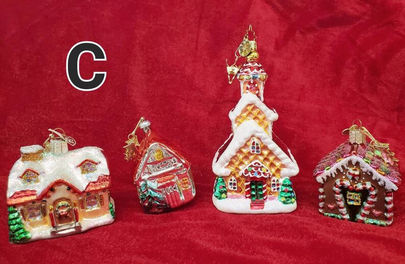 K&ouml;nnte beinhalten: Vier gl&auml;serne Weihnachtsbaumschmuckst&uuml;cke in Form von H&auml;usern. Die Schmuckst&uuml;cke sind mit Lebkuchendetails, Zuckerstangen und Schnee verziert. Die Schmuckst&uuml;cke befinden sich auf einem roten Hintergrund.