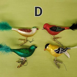 May include: Four glass bird ornaments with feather tails. The birds are red, green, white, and yellow with black accents. The ornaments have a clip on the bottom for hanging.