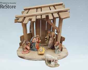 May include: A wooden nativity scene with figures of Mary, Joseph, baby Jesus, and two angels. The scene is set in a stable with a thatched roof and a manger. There are also two sheep in the scene.