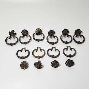 May include: A collection of 13 antique-style, ornate, metal drawer pulls in a variety of shapes and sizes. The pulls are all in a brass finish and have a distressed look.