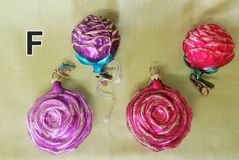 May include: Four glass Christmas ornaments shaped like roses. Two are pink with gold glitter, one is purple with gold glitter, and one is teal with gold glitter.