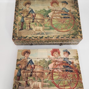 Könnte beinhalten: Vintage Holzklotz-Puzzle mit einer ländlichen Szene mit Kindern, Tieren und einem Wagen. Das Puzzle befindet sich in einer dekorativen Box mit einem passenden Bild auf dem Deckel. Die Blöcke sind so angeordnet, dass das vollständige Bild gezeigt wird.