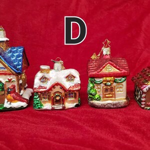 K&ouml;nnte beinhalten: Vier gl&auml;serne Weihnachtsbaumschmuckst&uuml;cke in Form von H&auml;usern. Die H&auml;user sind mit Schnee, Zuckerstangen und anderen festlichen Details verziert. Die Schmuckst&uuml;cke sind alle in verschiedenen Farben und Stilen gehalten. Der Text "Our New Home" befindet sich auf einem der Schmuckst&uuml;cke.