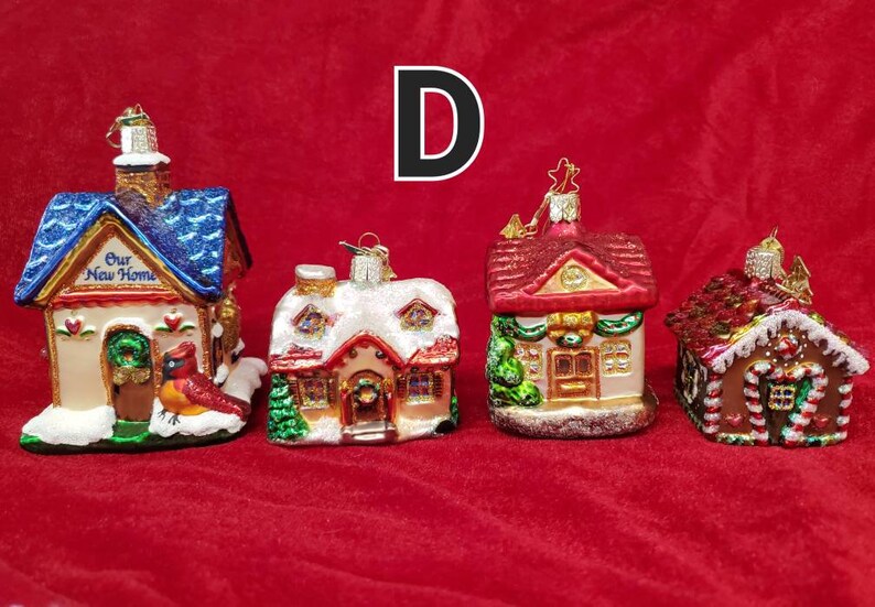 K&ouml;nnte beinhalten: Vier gl&auml;serne Weihnachtsbaumschmuckst&uuml;cke in Form von H&auml;usern. Die H&auml;user sind mit Schnee, Zuckerstangen und anderen festlichen Details verziert. Die Schmuckst&uuml;cke sind alle in verschiedenen Farben und Stilen gehalten. Der Text "Our New Home" befindet sich auf einem der Schmuckst&uuml;cke.